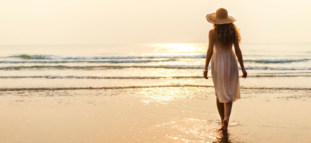 Female wearing a sun hat paddling in sea water enjoying lovely sunshine
