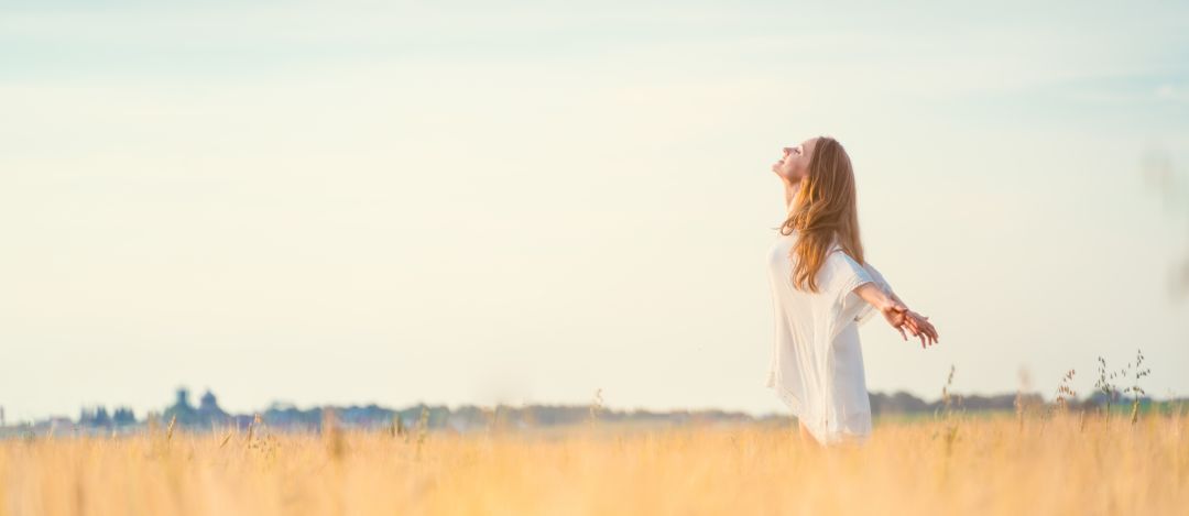 Young female standing in a field enjoying freedom in the sunshine